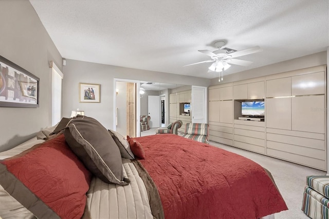 bedroom with light carpet, a textured ceiling, ceiling fan, and connected bathroom