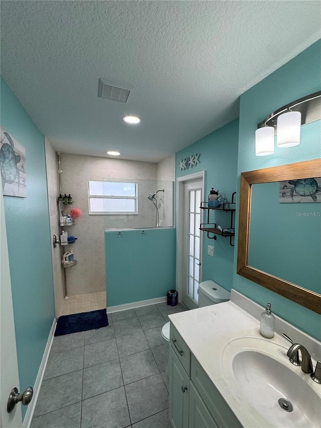 bathroom with tile patterned floors, vanity, a textured ceiling, tiled shower, and toilet