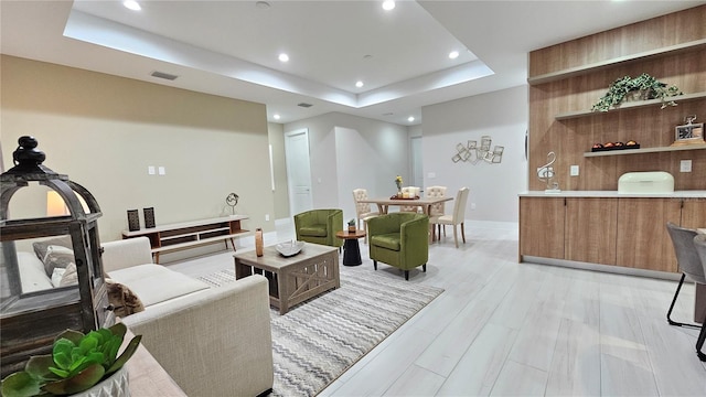 living room with light hardwood / wood-style floors and a tray ceiling