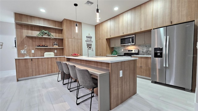 kitchen with decorative backsplash, stainless steel appliances, a kitchen island with sink, sink, and decorative light fixtures