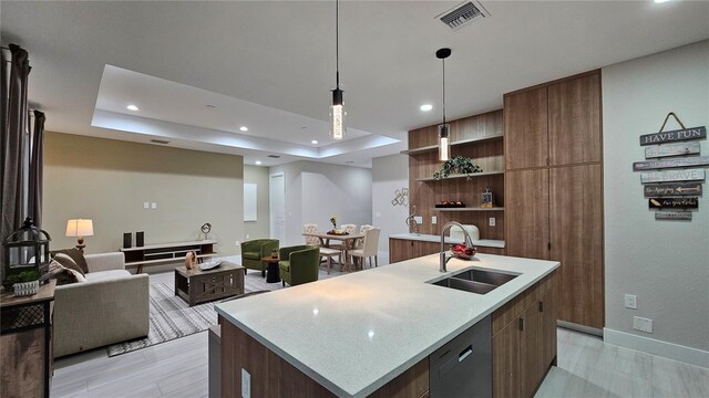 kitchen featuring sink, a kitchen island with sink, hanging light fixtures, and a tray ceiling