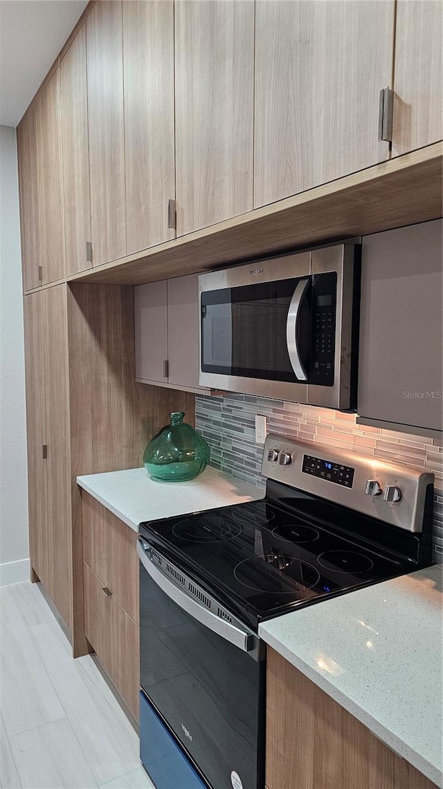 kitchen with light stone counters, light brown cabinetry, backsplash, and appliances with stainless steel finishes