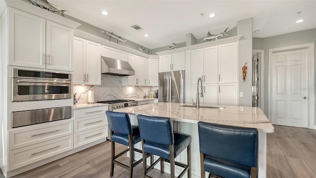 kitchen with white cabinets, an island with sink, exhaust hood, and appliances with stainless steel finishes