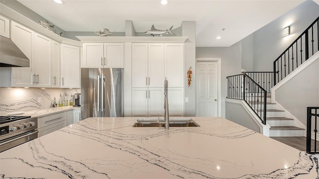 kitchen featuring light stone counters, sink, white cabinets, and premium appliances