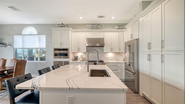 kitchen with light stone countertops, high quality fridge, a breakfast bar, ventilation hood, and a kitchen island with sink