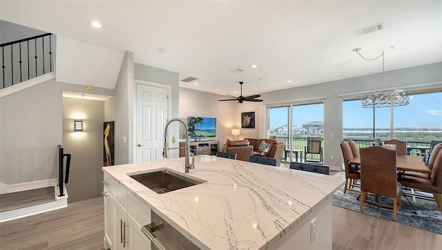 kitchen with sink, hanging light fixtures, light stone countertops, an island with sink, and white cabinetry