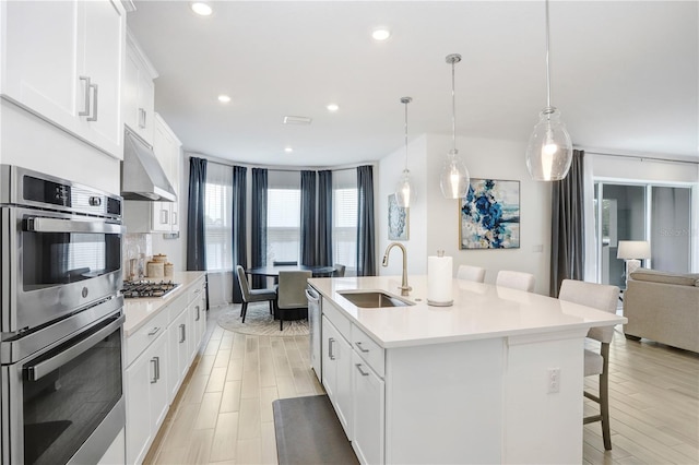 kitchen with sink, stainless steel appliances, a kitchen breakfast bar, extractor fan, and a kitchen island with sink