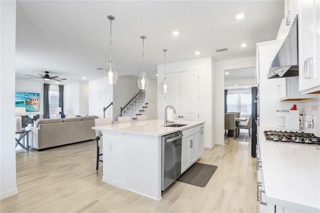 kitchen with stainless steel appliances, sink, white cabinetry, hanging light fixtures, and an island with sink