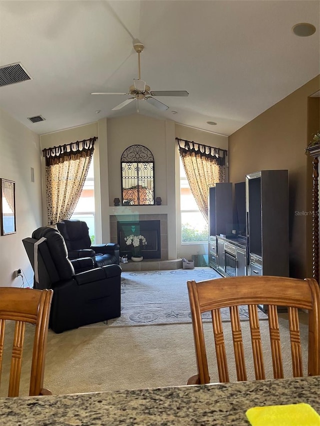 carpeted living room featuring a tile fireplace, vaulted ceiling, and ceiling fan