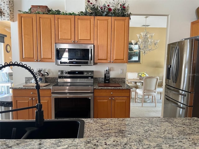 kitchen with light stone counters, a notable chandelier, and appliances with stainless steel finishes