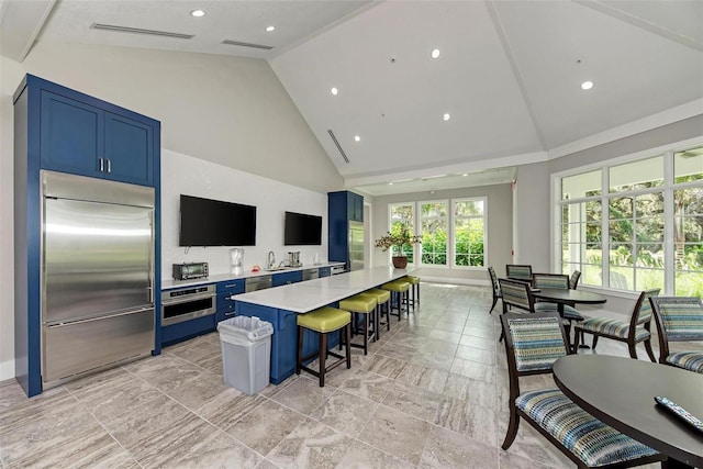 1387 Still River Dr, Venice, FL 34293 - kitchen featuring stainless steel appliances, blue cabinetry, light countertops, a kitchen bar, and high vaulted ceiling