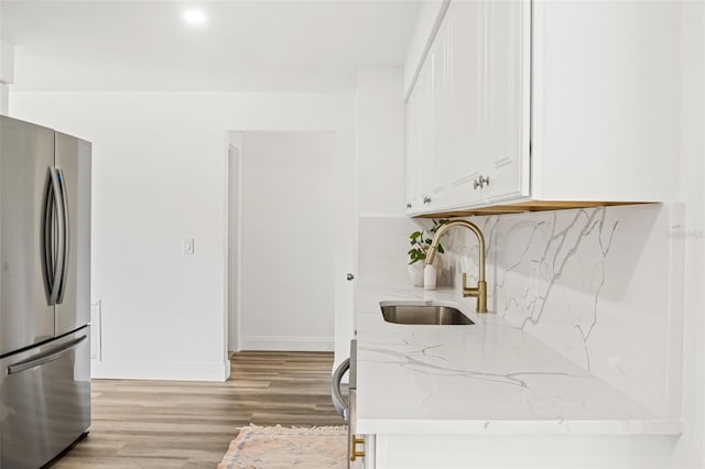 kitchen with stainless steel fridge, light stone counters, sink, light hardwood / wood-style flooring, and white cabinets