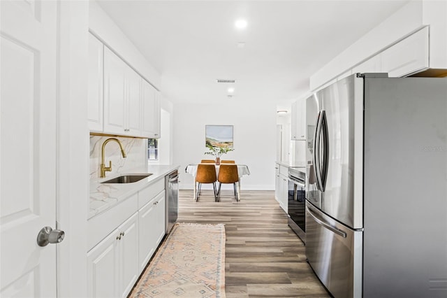 kitchen with sink, backsplash, appliances with stainless steel finishes, white cabinets, and hardwood / wood-style flooring