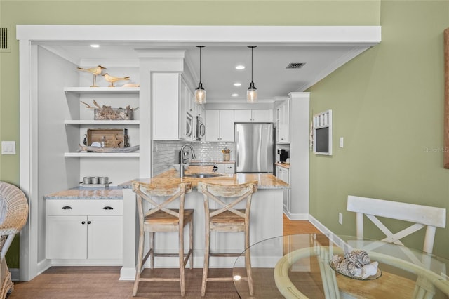 kitchen with stainless steel refrigerator, white cabinetry, sink, hanging light fixtures, and light stone counters