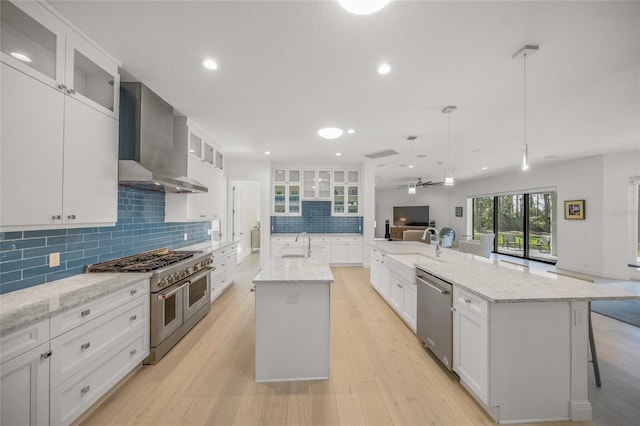 kitchen with white cabinetry, a center island with sink, stainless steel appliances, and wall chimney range hood