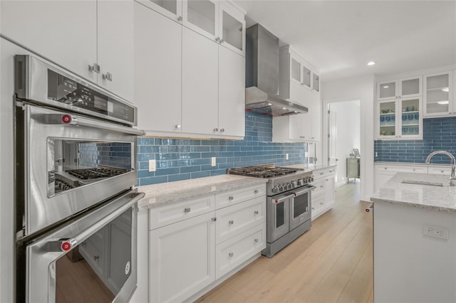 kitchen with sink, wall chimney exhaust hood, light hardwood / wood-style floors, white cabinets, and appliances with stainless steel finishes