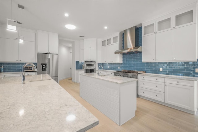 kitchen featuring white cabinets, appliances with stainless steel finishes, a kitchen island with sink, and wall chimney exhaust hood