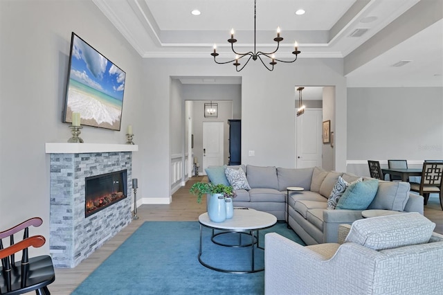 living room featuring a raised ceiling, a stone fireplace, light hardwood / wood-style floors, and a notable chandelier