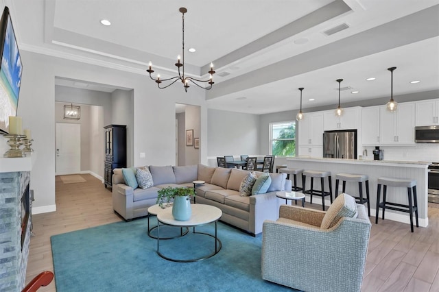 living room featuring a tray ceiling, a chandelier, and light wood-type flooring