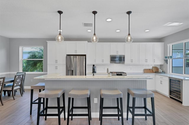 8089 Sandstar Way, Sarasota, FL 34240 - kitchen with stainless steel appliances, wine cooler, decorative backsplash, white cabinets, and light wood-style flooring