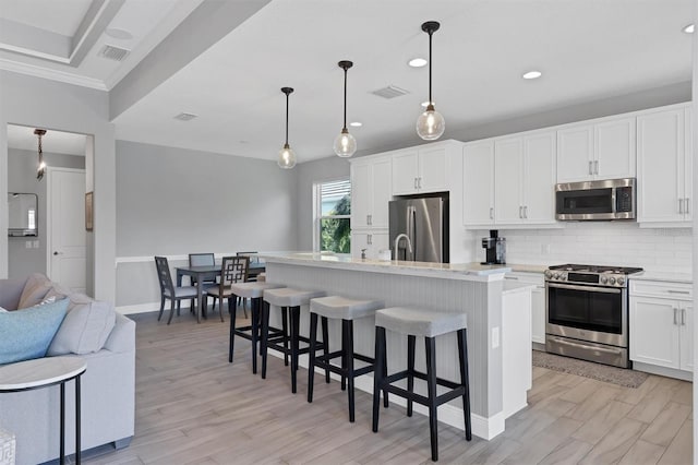 kitchen featuring hanging light fixtures, stainless steel appliances, white cabinetry, and a kitchen island with sink