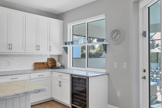 8089 Sandstar Way, Sarasota, FL 34240 - kitchen featuring wine cooler, white cabinets, tasteful backsplash, light stone counters, and light wood-style flooring