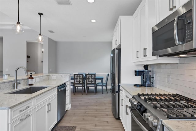 8089 Sandstar Way, Sarasota, FL 34240 - kitchen with stainless steel appliances, white cabinets, tasteful backsplash, light wood finished floors, and pendant lighting
