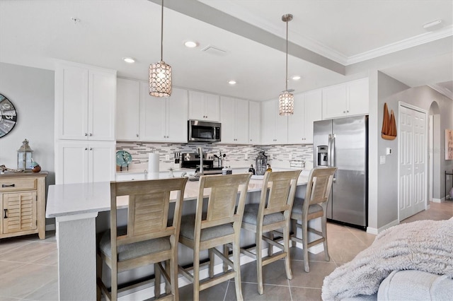 kitchen featuring white cabinets, appliances with stainless steel finishes, a center island with sink, and pendant lighting