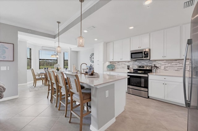 kitchen featuring white cabinetry, decorative light fixtures, a kitchen island with sink, appliances with stainless steel finishes, and ornamental molding