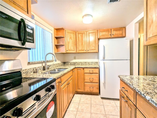 kitchen with sink, light tile patterned floors, a textured ceiling, light stone countertops, and appliances with stainless steel finishes