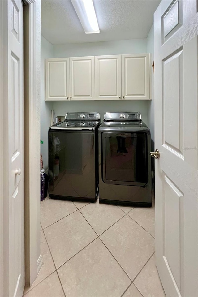 washroom with cabinets, light tile patterned floors, a textured ceiling, and washing machine and clothes dryer