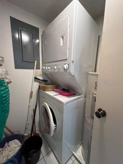 laundry room with light tile patterned floors, electric panel, stacked washer and clothes dryer, and water heater