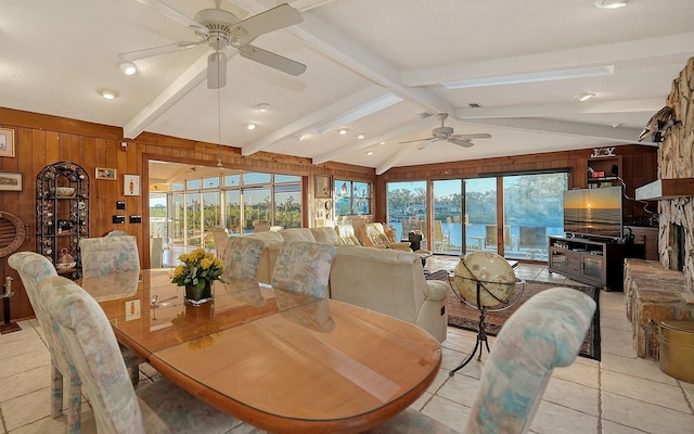 dining area featuring lofted ceiling with beams, a healthy amount of sunlight, ceiling fan, and wood walls