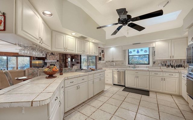 kitchen featuring sink, tile counters, stainless steel dishwasher, and white cabinets