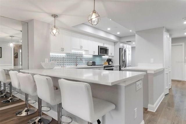 kitchen with a breakfast bar, stainless steel appliances, pendant lighting, white cabinets, and light hardwood / wood-style floors