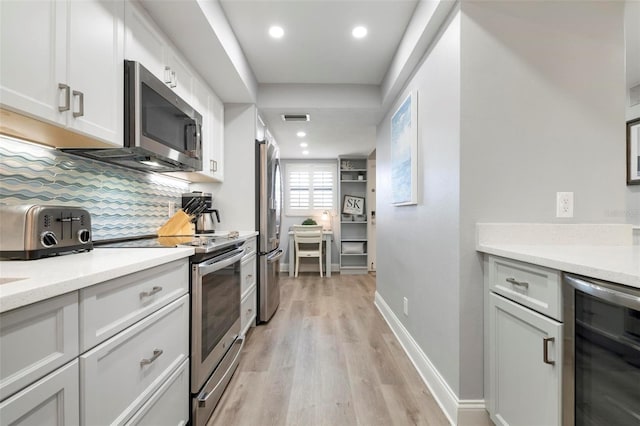 kitchen featuring beverage cooler, tasteful backsplash, light stone counters, light hardwood / wood-style flooring, and appliances with stainless steel finishes