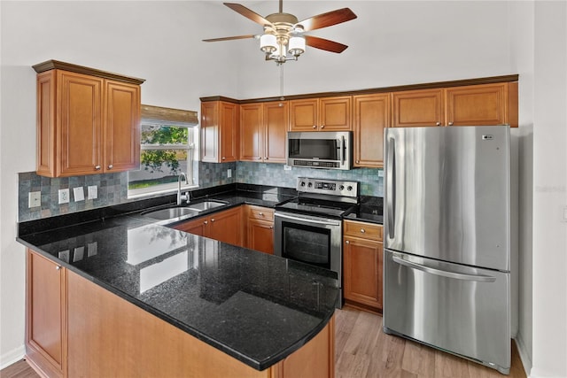 kitchen with light wood-type flooring, backsplash, dark stone counters, stainless steel appliances, and sink