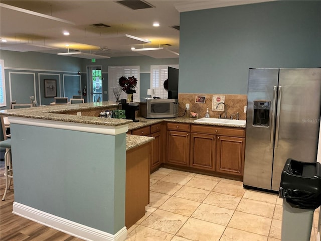 kitchen with light stone countertops, sink, stainless steel appliances, backsplash, and kitchen peninsula