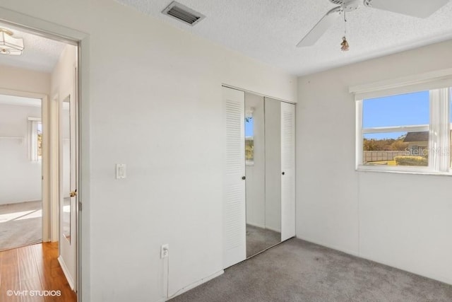 unfurnished bedroom with ceiling fan, light colored carpet, a textured ceiling, and a closet