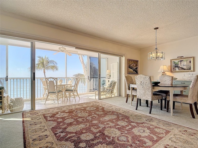 carpeted dining space with ceiling fan with notable chandelier, a textured ceiling, a water view, and crown molding