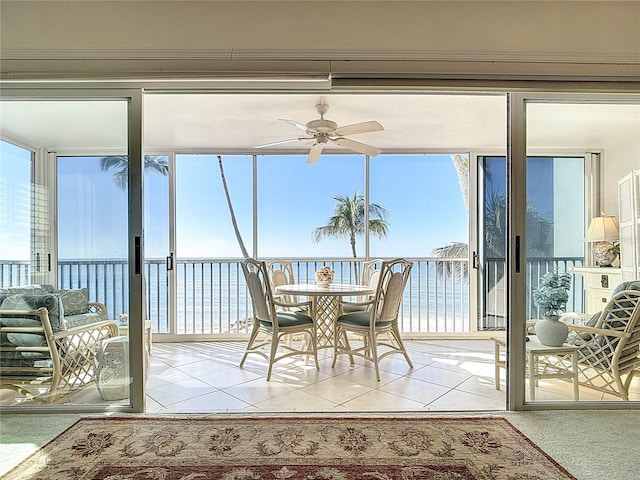 sunroom with ceiling fan and a water view