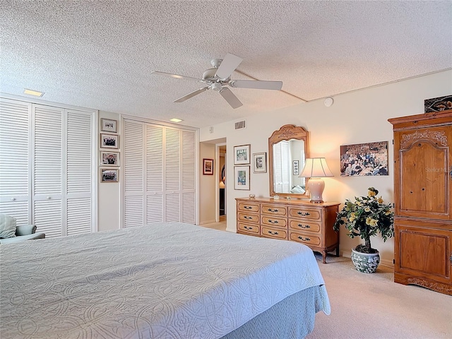 bedroom featuring multiple closets, ceiling fan, light carpet, and a textured ceiling