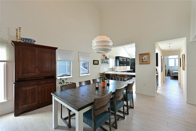 dining room with light wood-type flooring, sink, and a high ceiling