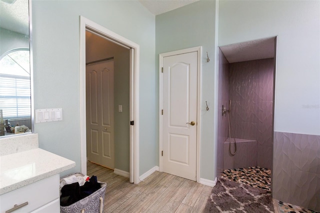 bathroom with hardwood / wood-style flooring, vanity, and a tile shower