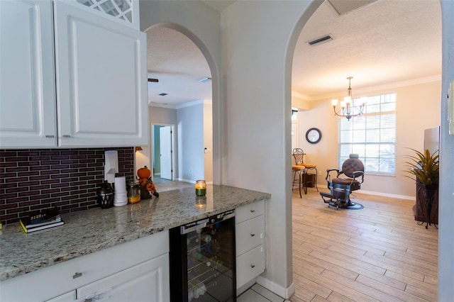 kitchen featuring pendant lighting, white cabinetry, wine cooler, and light stone counters