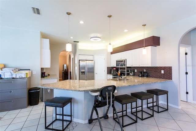 kitchen with white cabinets, light tile patterned floors, appliances with stainless steel finishes, decorative light fixtures, and kitchen peninsula