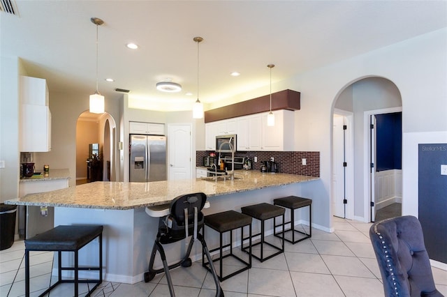 kitchen with appliances with stainless steel finishes, sink, light stone counters, white cabinetry, and decorative light fixtures