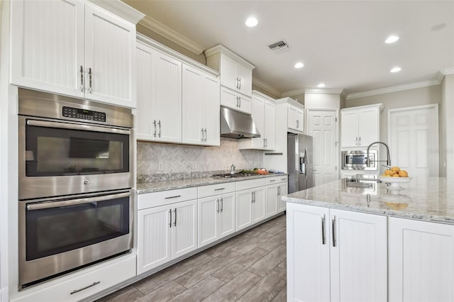 kitchen with white cabinets, crown molding, light stone counters, and stainless steel appliances