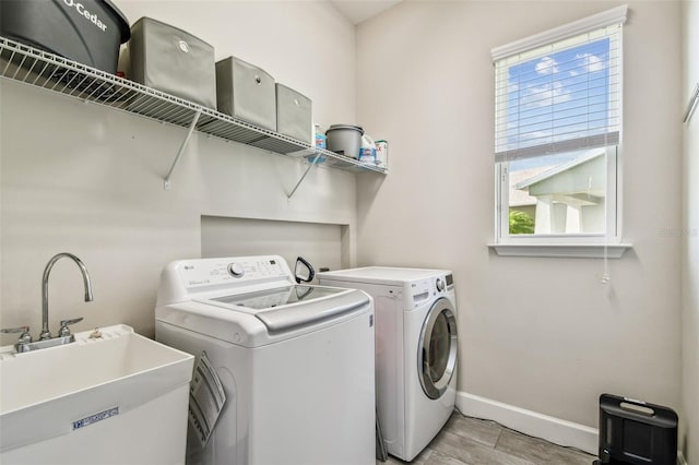 clothes washing area featuring separate washer and dryer, sink, and light wood-type flooring