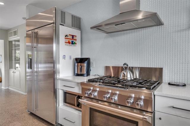 kitchen with light stone countertops, backsplash, high end appliances, and wall chimney range hood